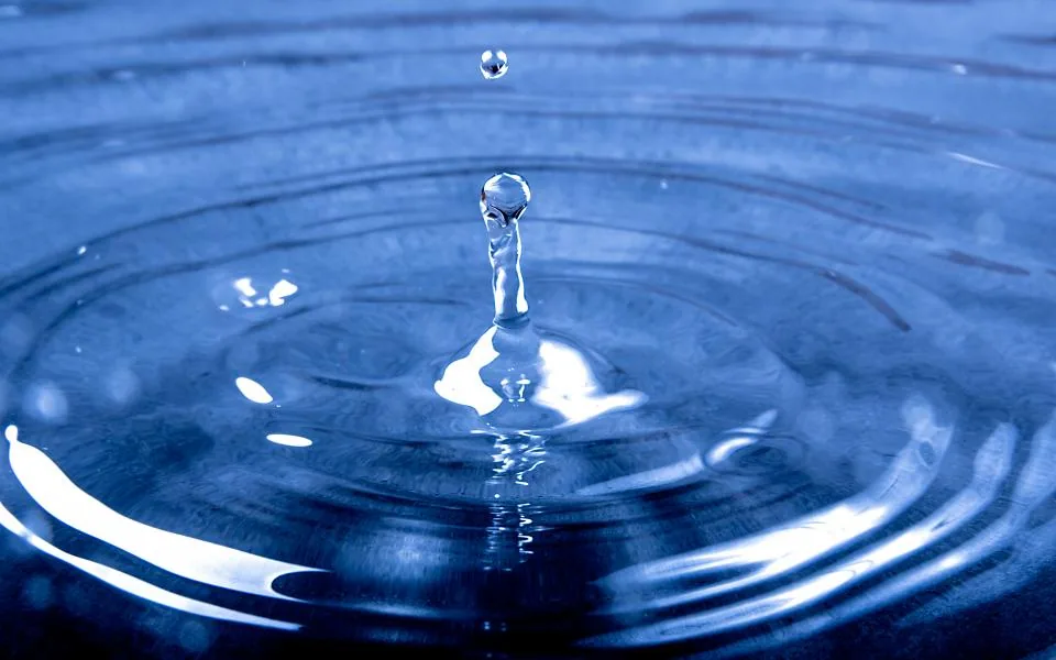 A single water droplet striking a deep blue surface